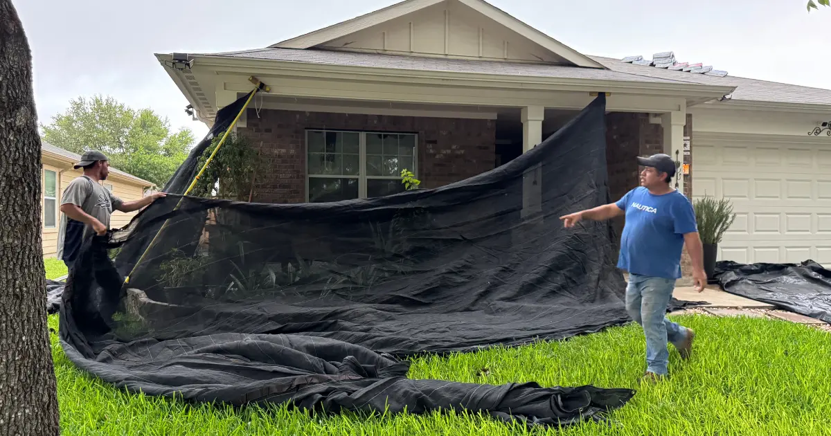Black safety netting raised around the perimeter of a house during roof work.