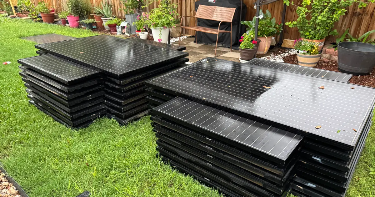 Solar panels stacked and stored on a lawn while a roof is being replaced.